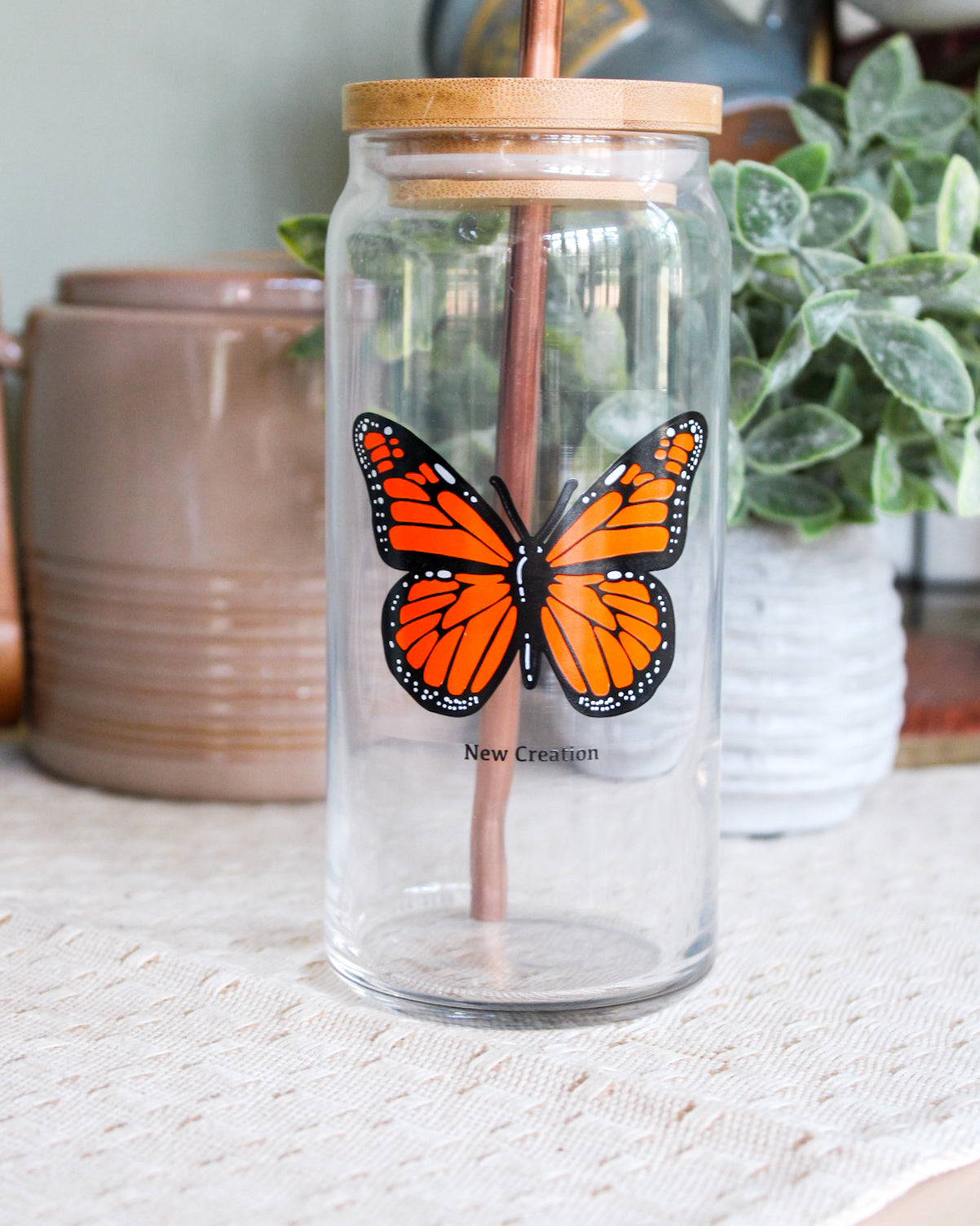 Clear glass coffee cup with butterfly design and wooden lid on a light surface.