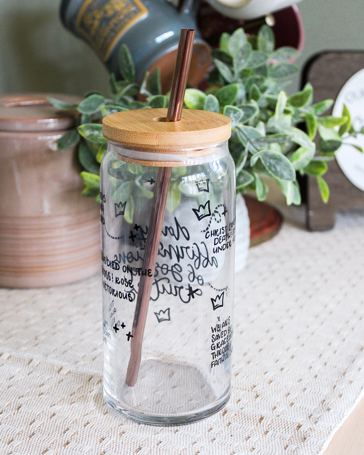 Clear glass jar with bamboo lid and straw on a textured surface with plants in the background