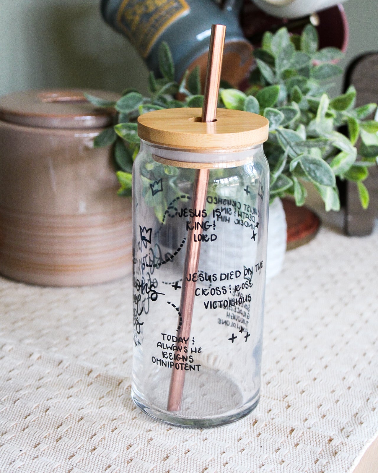 Glass tumbler with straw and wooden lid on a textured surface with plants in the background