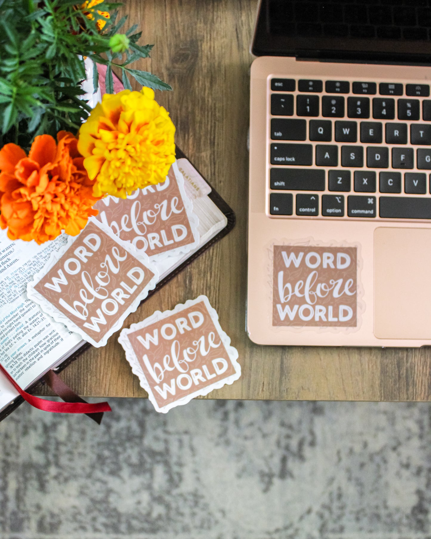Laptop with 'Word before World' stickers on a table with Bible and flowers.
