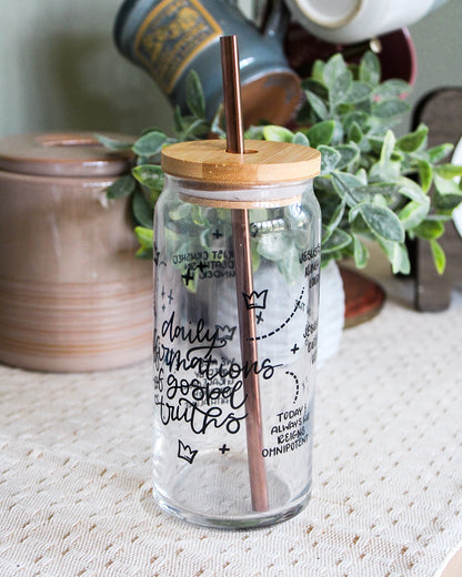 Clear glass jar with wooden lid and straw, featuring text, on a textured surface with plants in the background.