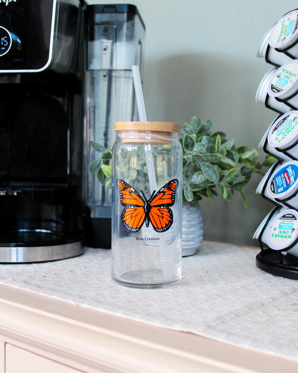 Clear glass jar with butterfly design on a kitchen counter next to a coffee maker.
